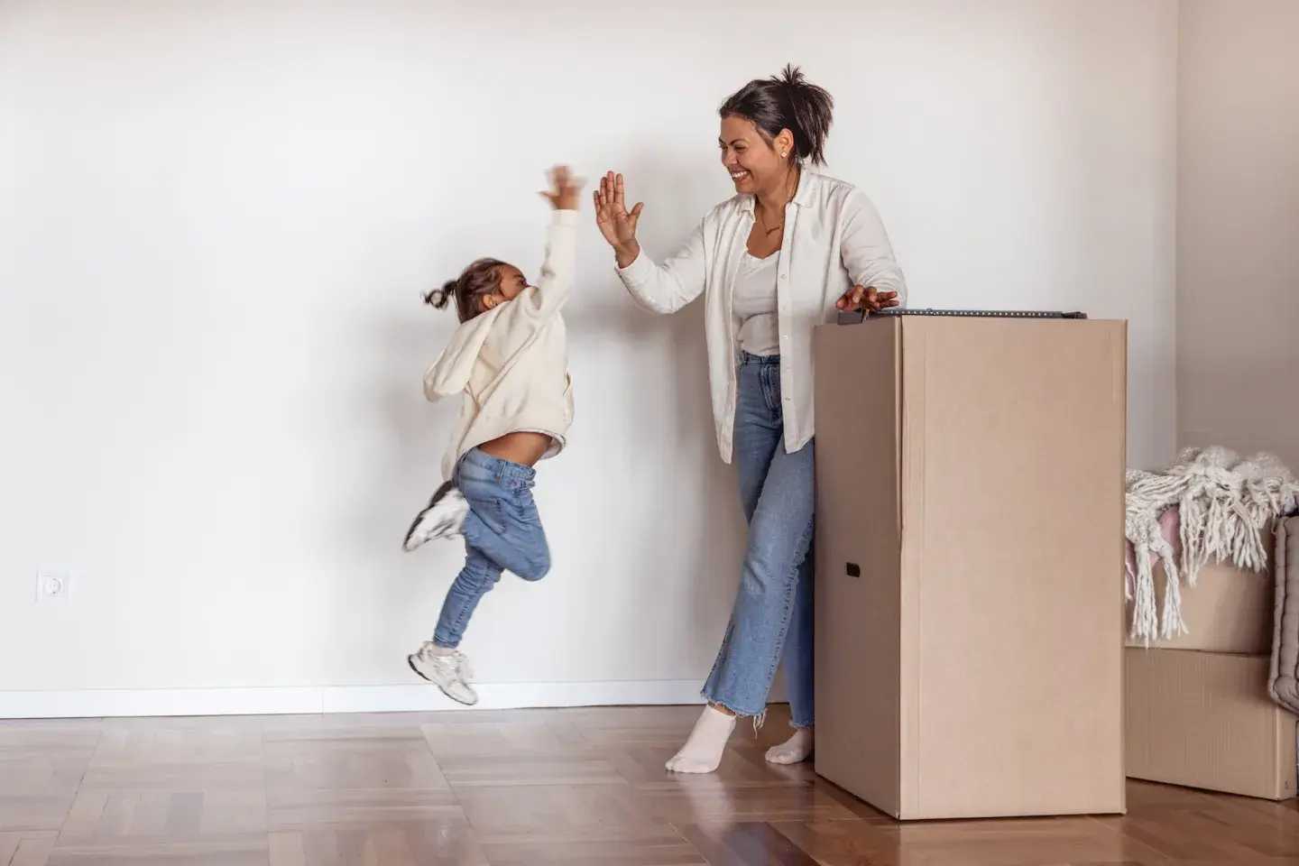 Mother and young daughter high-fiving joyfully next to a large cardboard moving box. Mother and young daughter high-fiving joyfully next to a large cardboard moving box.
