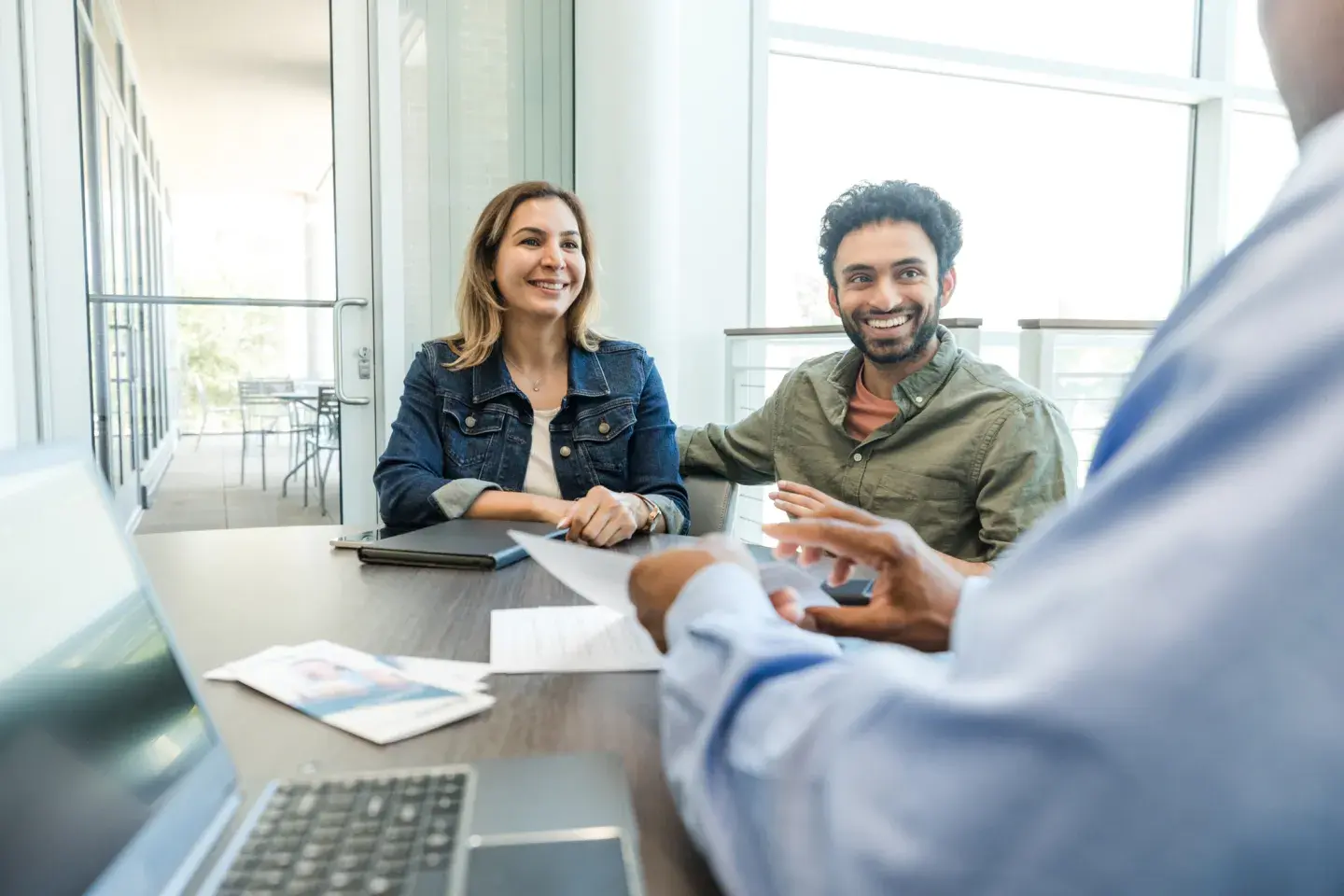 Smiling couple shaking hands with a professional across a desk in a bright office setting. Smiling couple shaking hands with a professional across a desk in a bright office setting.