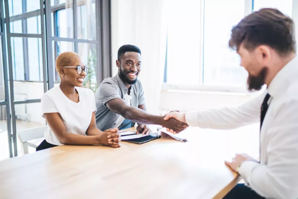 excited young couple shaking hands with business man after signing contract excited young couple shaking hands with business man after signing contract