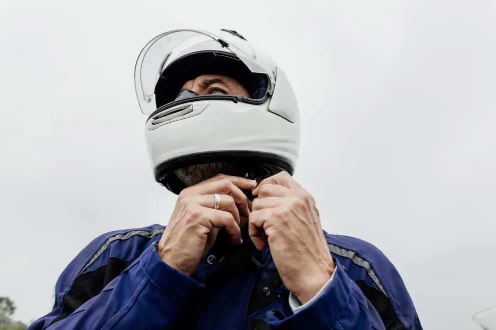 Person wearing helmet and blue jacket adjusting the helmet with both hands. Person wearing helmet and blue jacket adjusting the helmet with both hands.