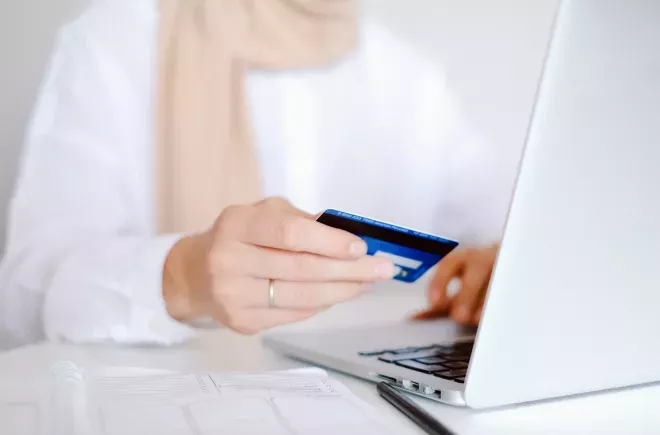 close up of person holding credit card out in one hand while shopping on laptop close up of person holding credit card out in one hand while shopping on laptop