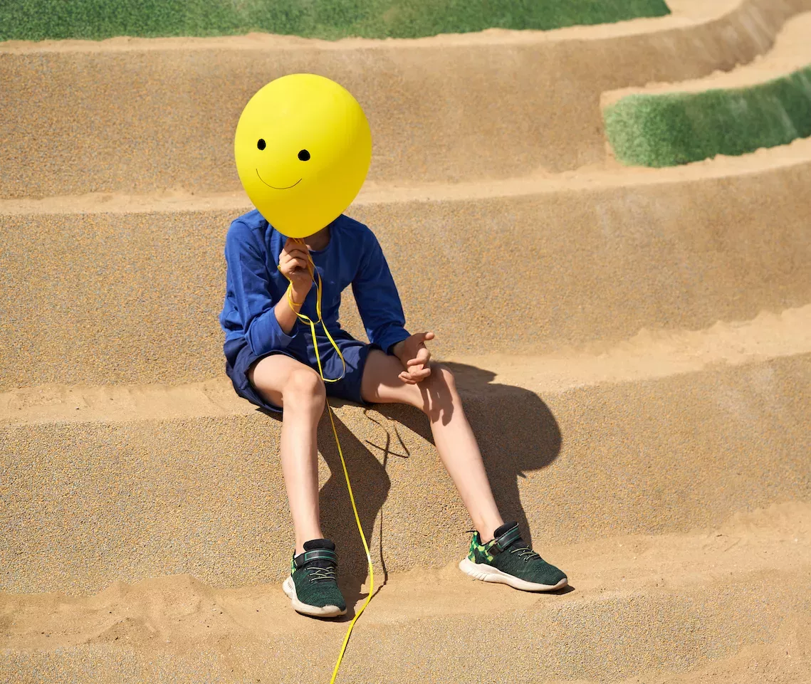 Kid holding a happy face balloon over his face Kid holding a happy face balloon over his face