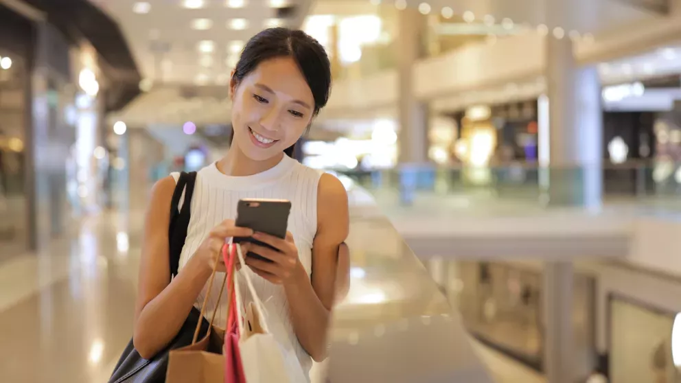 smiling woman at mall with shopping bags looking at cell phone smiling woman at mall with shopping bags looking at cell phone