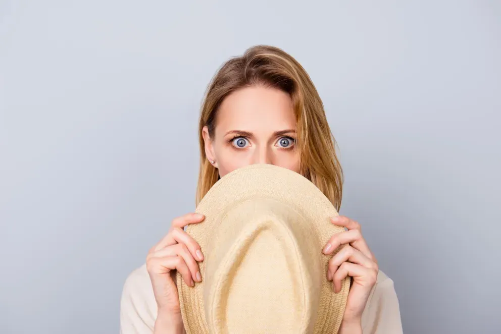 woman with shocked expression hiding behind hat woman with shocked expression hiding behind hat