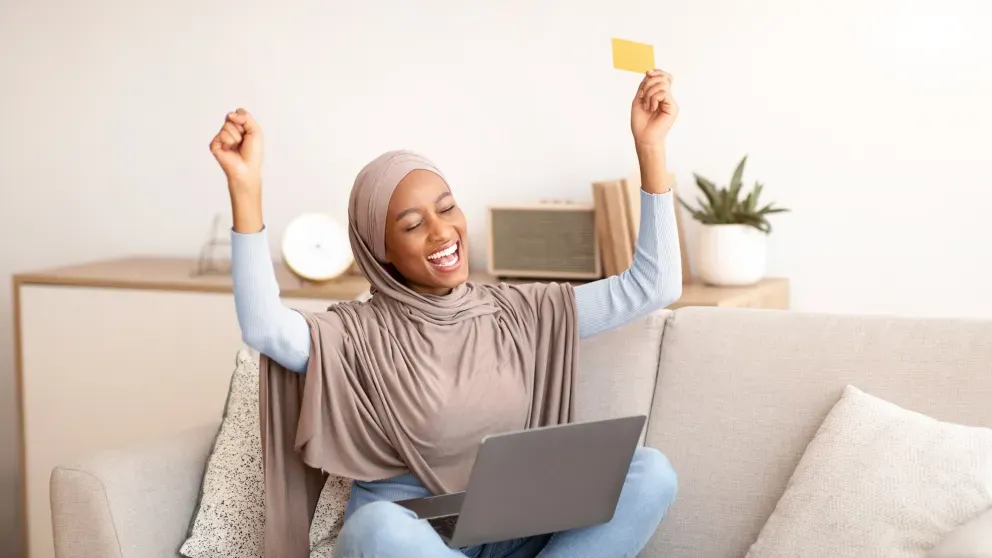 Excited Muslim woman holding card and laptop Excited Muslim woman holding card and laptop