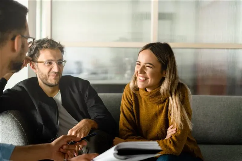 Woman smiling at man helping with paperwork, another man beside her gazing at the woman Woman smiling at man helping with paperwork, another man beside her gazing at the woman