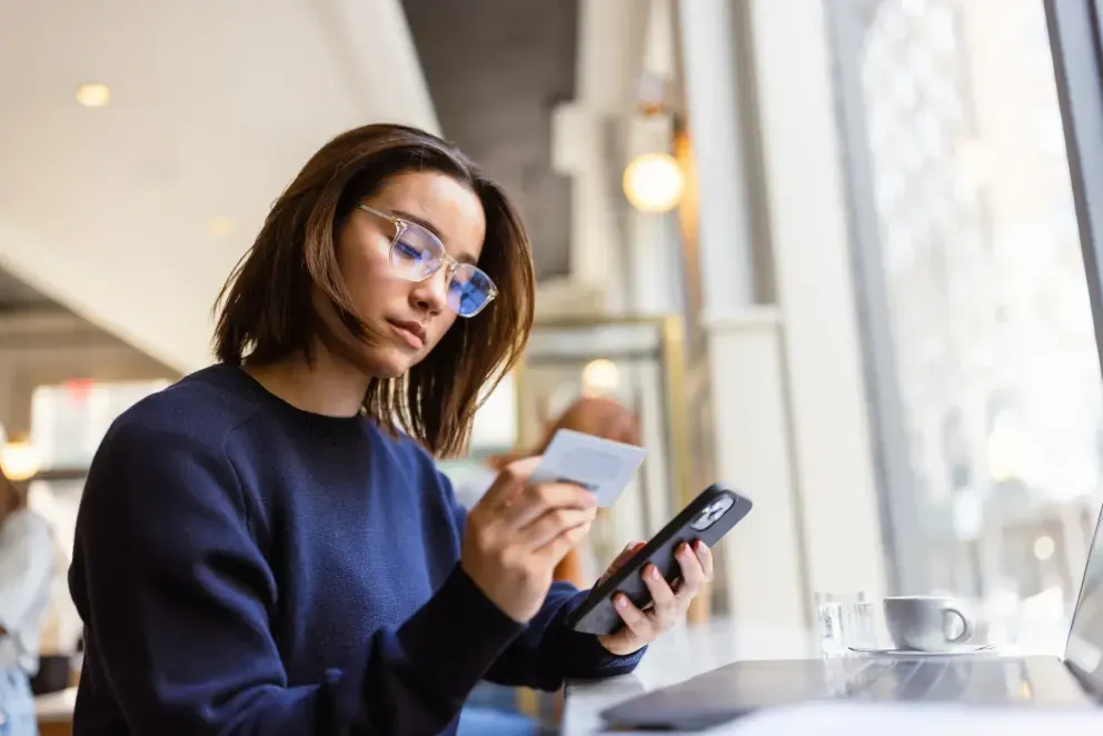 Young woman in blue sweater holding a credit card and smartphone indoors. Young woman in blue sweater holding a credit card and smartphone indoors.