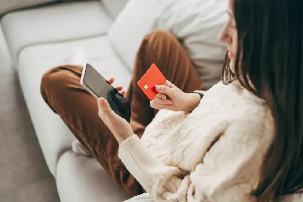 Woman sitting on a couch holding a smartphone and a red credit card. Woman sitting on a couch holding a smartphone and a red credit card.