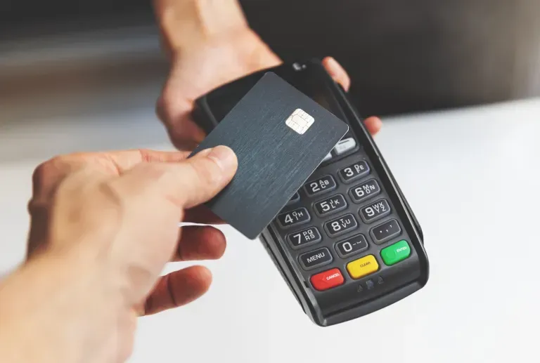 Person's hand inserting credit card into black payment terminal with colorful buttons Person's hand inserting credit card into black payment terminal with colorful buttons