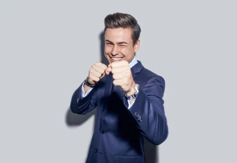 Man in blue suit smiling and posing with raised fists against a gray background. Man in blue suit smiling and posing with raised fists against a gray background.