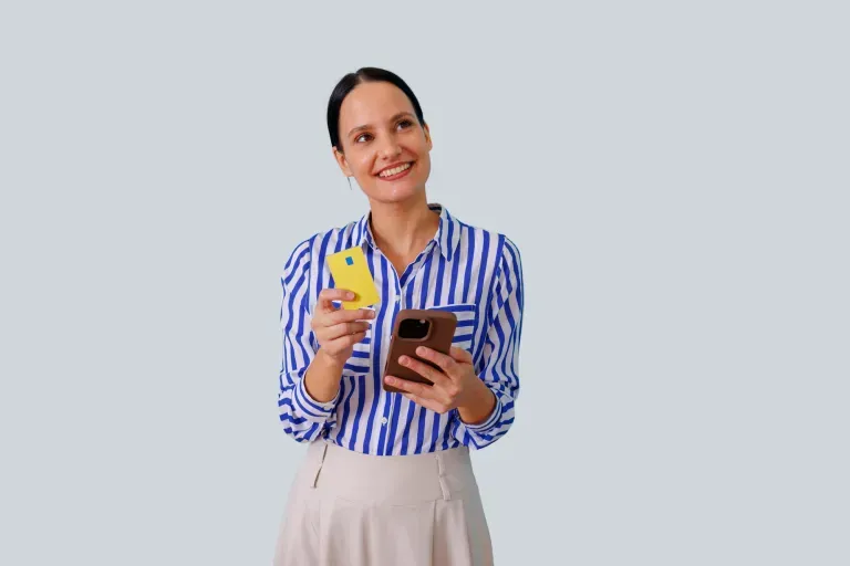Smiling young woman in striped shirt holding a drink and smartphone against a light gray background. Smiling young woman in striped shirt holding a drink and smartphone against a light gray background.