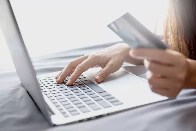 Person holding a card and using a laptop Person holding a card and using a laptop