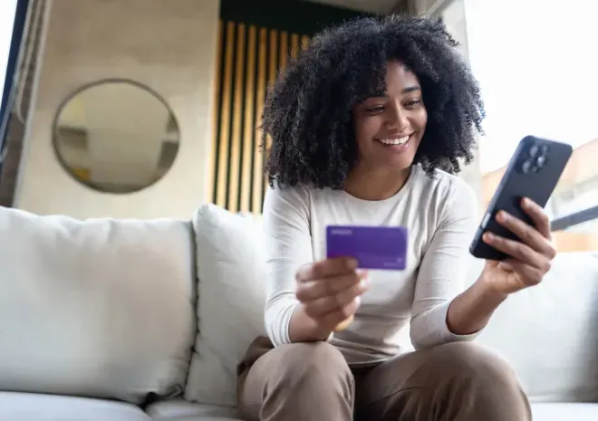 Smiling woman sitting on a couch, holding a purple credit card and smartphone. Smiling woman sitting on a couch, holding a purple credit card and smartphone.