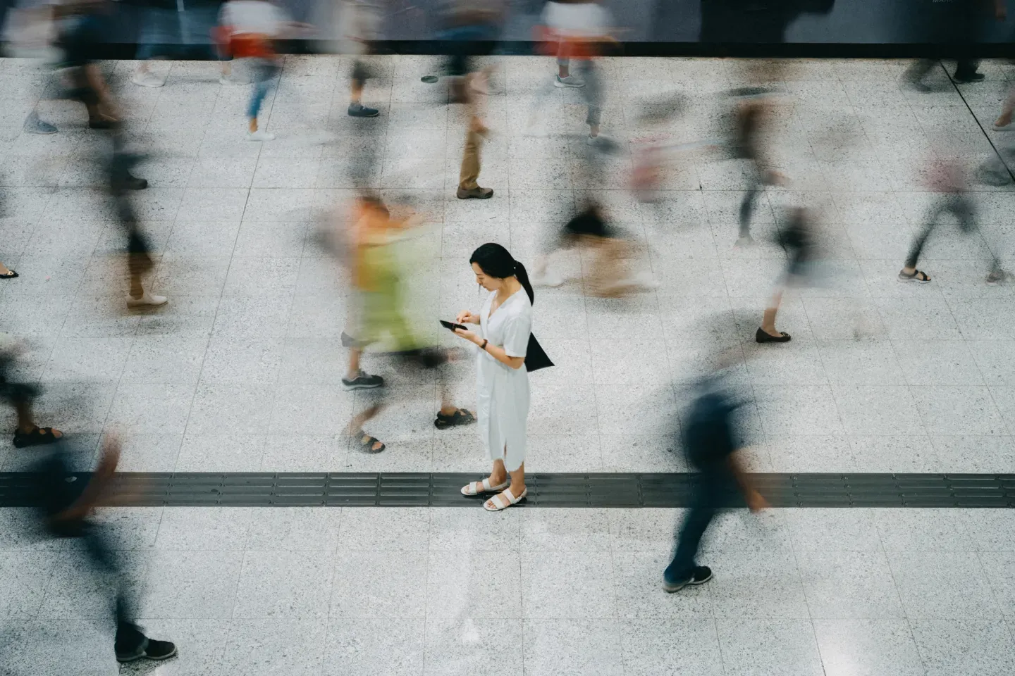Woman standing still looking at phone amid blurred crowd of rushing pedestrians, aerial view. Woman standing still looking at phone amid blurred crowd of rushing pedestrians, aerial view.