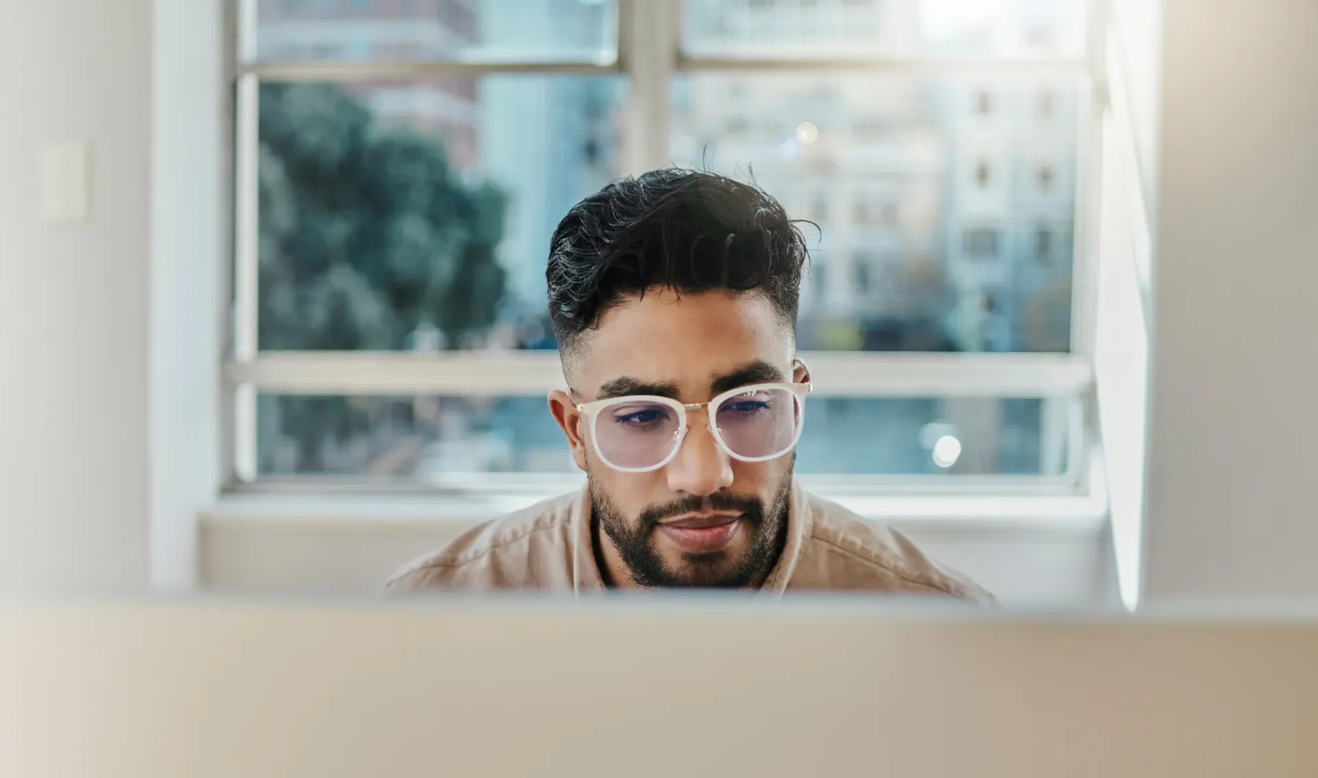 Young man with glasses focused on a computer screen in a bright office setting. Young man with glasses focused on a computer screen in a bright office setting.