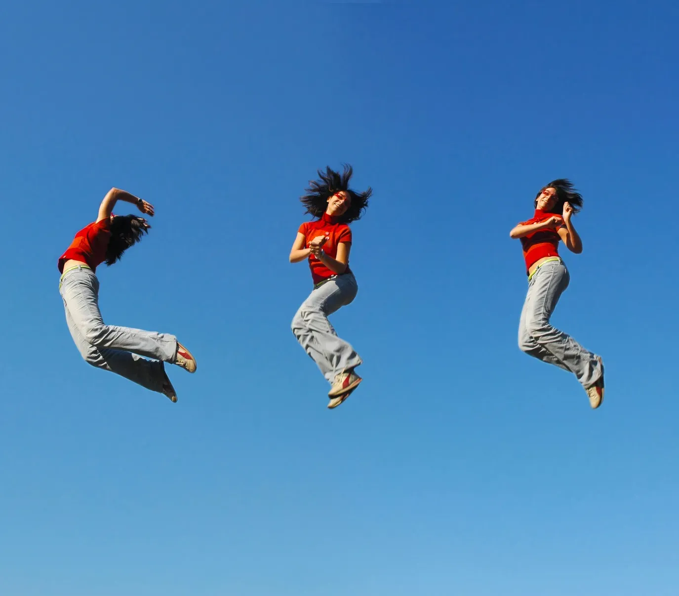 Three sequential shots of a woman in a red top jumping energetically against a clear blue sky. Three sequential shots of a woman in a red top jumping energetically against a clear blue sky.