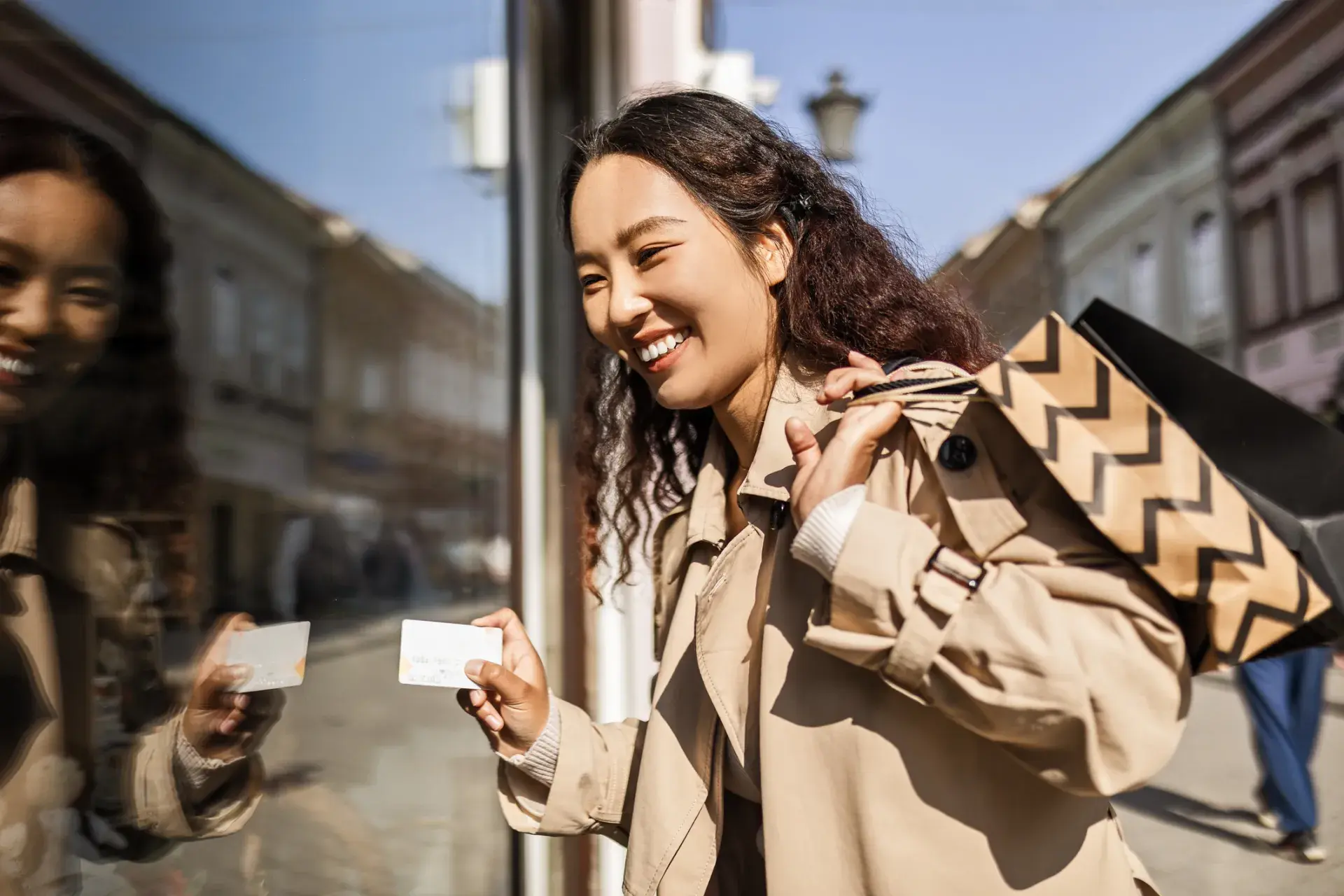 woman holding shopping backs and a credit card next to a window with her reflection woman holding shopping backs and a credit card next to a window with her reflection